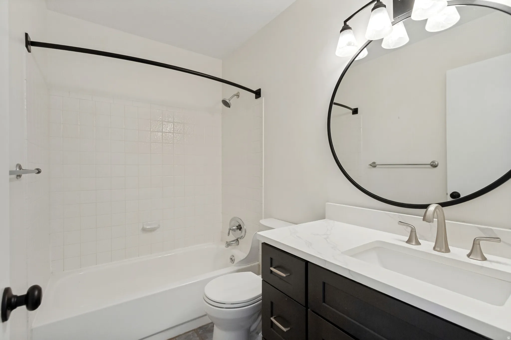 White subway tile bath surround, dark wood-finish vanity with white countertop, round black-framed mirror, and brushed nickel fixtures