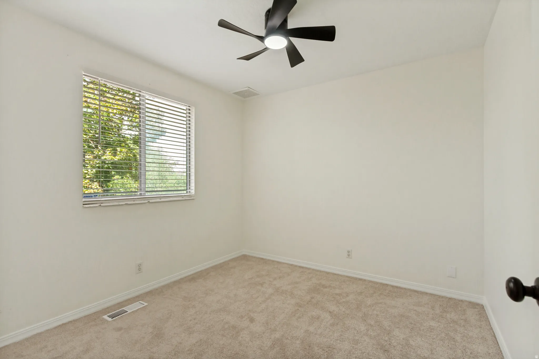 Neutral wall paint, carpeted flooring, window with blinds, and a ceiling fan with integrated lighting