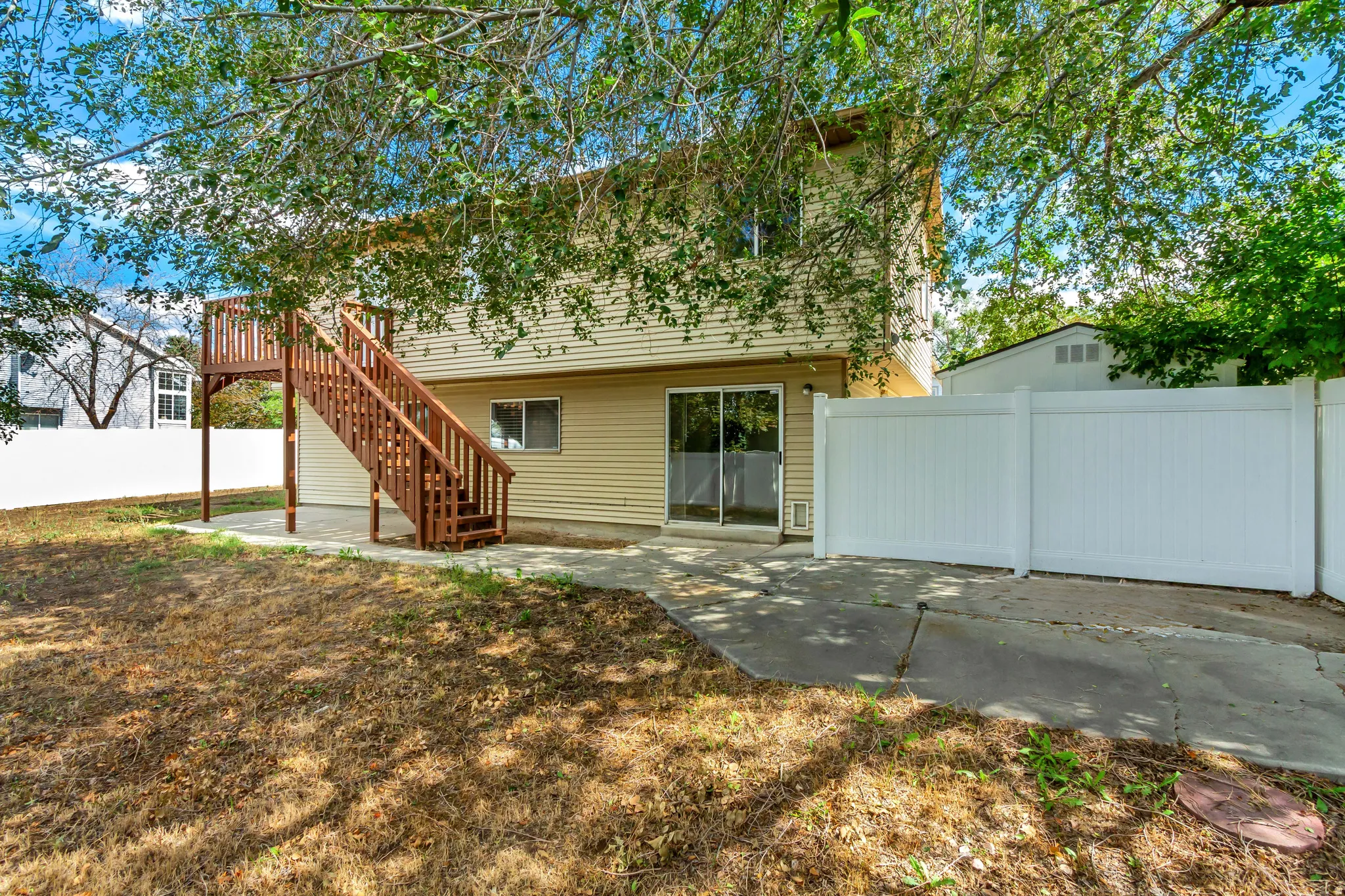 Rear exterior with siding, sliding glass door, elevated wood deck with stairs, and white privacy fencing
