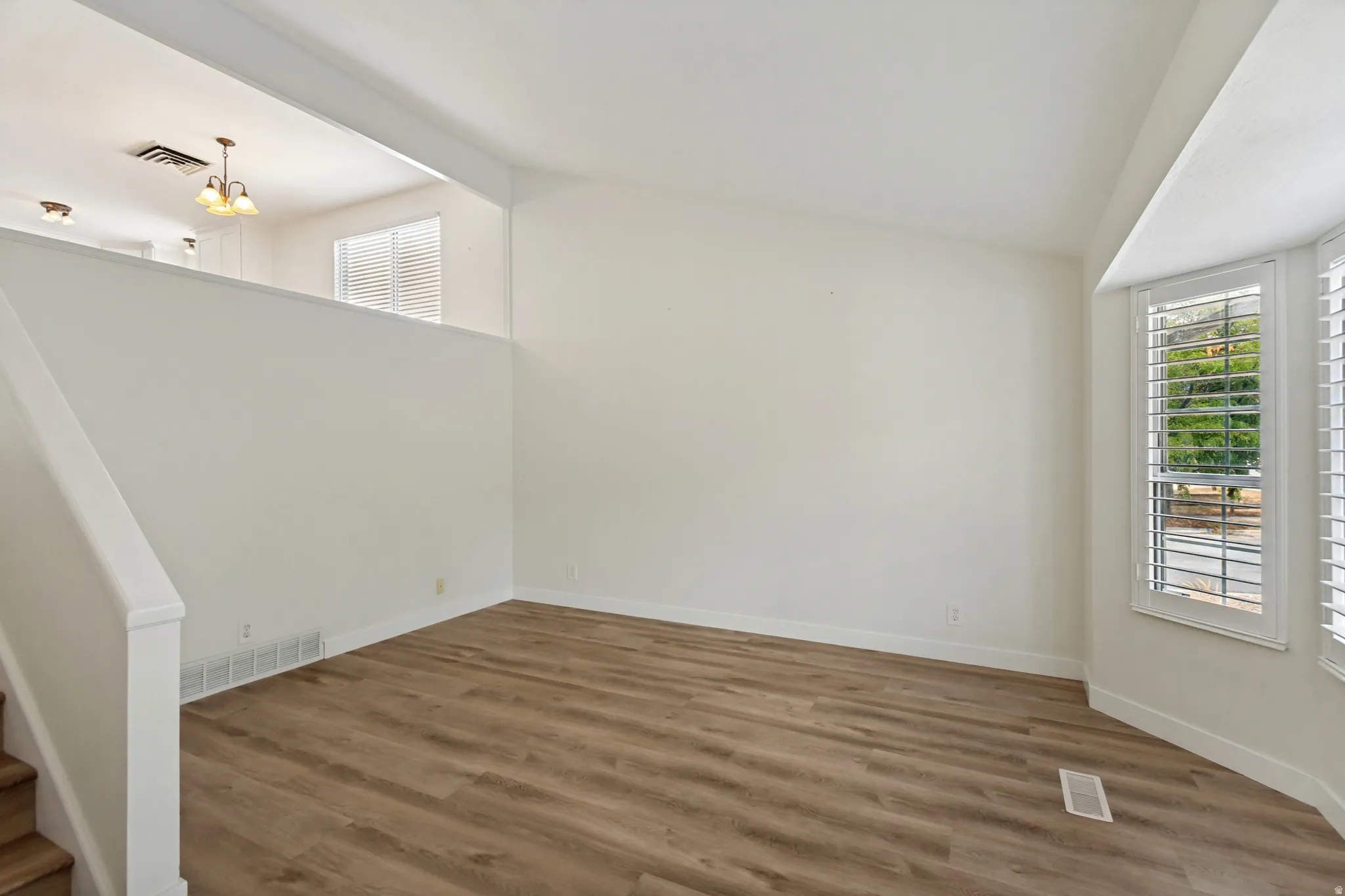 Interior space featuring wood-finish flooring, white walls, and a bay window with plantation shutters