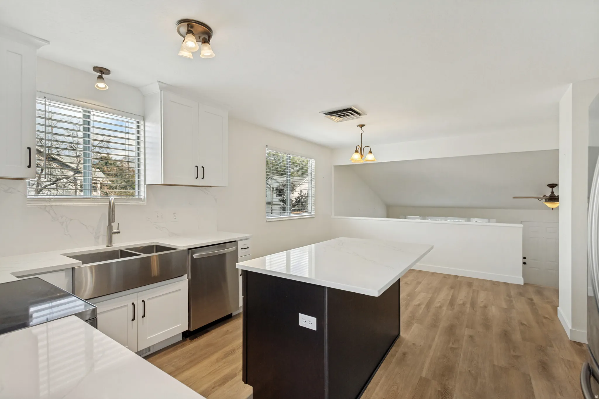 Contemporary kitchen featuring white cabinetry, a large farmhouse-style sink, stainless steel appliances, and a central island with a white countertop