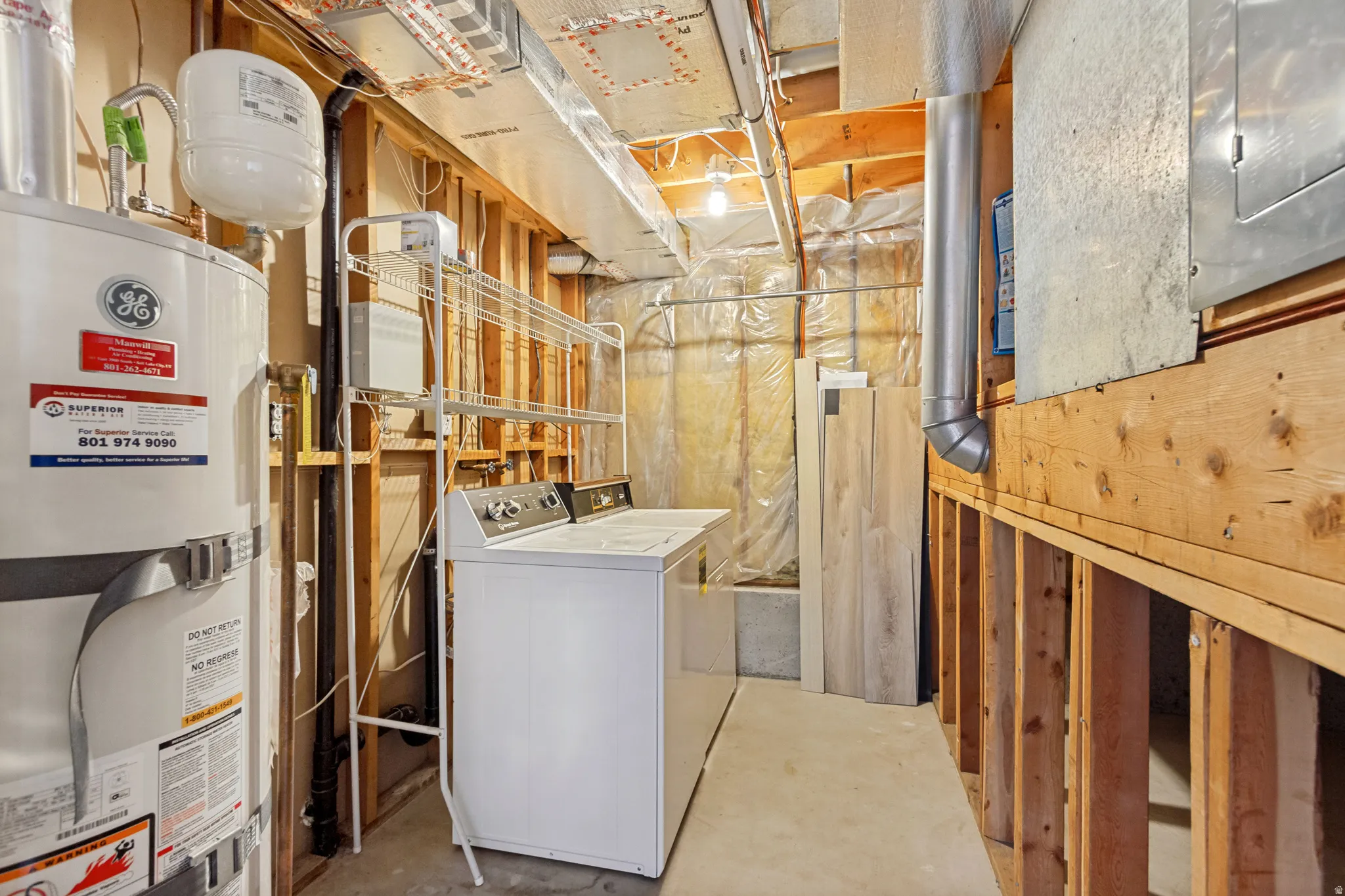 Utility room with exposed wood framing, concrete flooring, and water heater