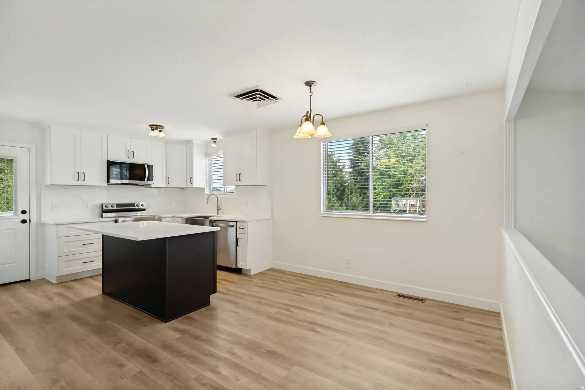 Kitchen featuring an island, stainless steel appliances, wood-finish flooring, white cabinetry, and a window with blinds