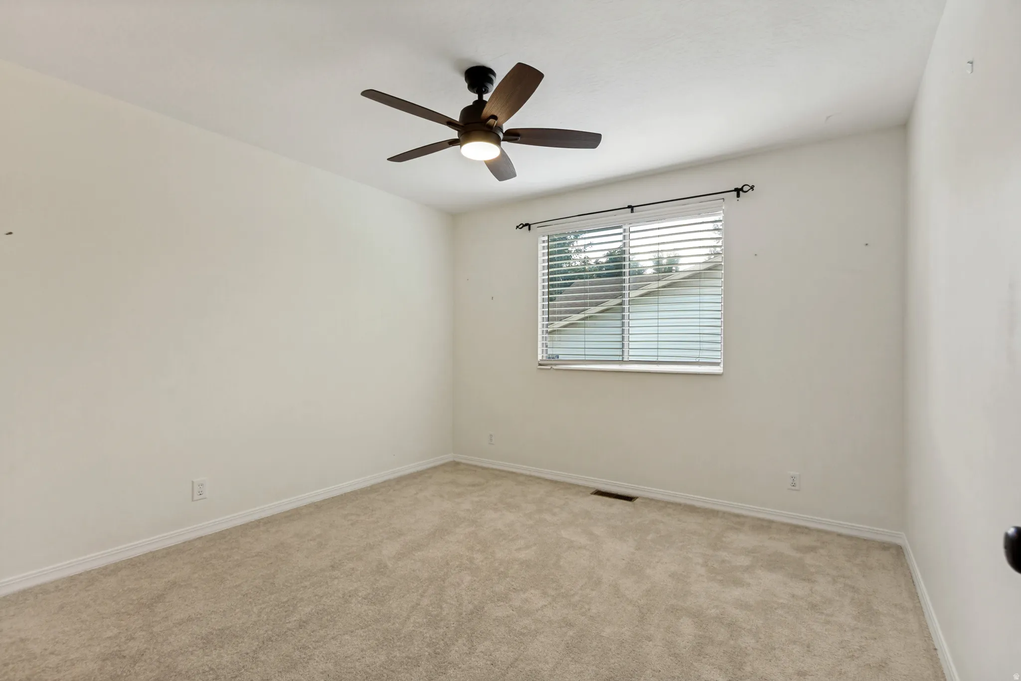 Carpeted room featuring a ceiling fan with integrated lighting and a window with horizontal blinds