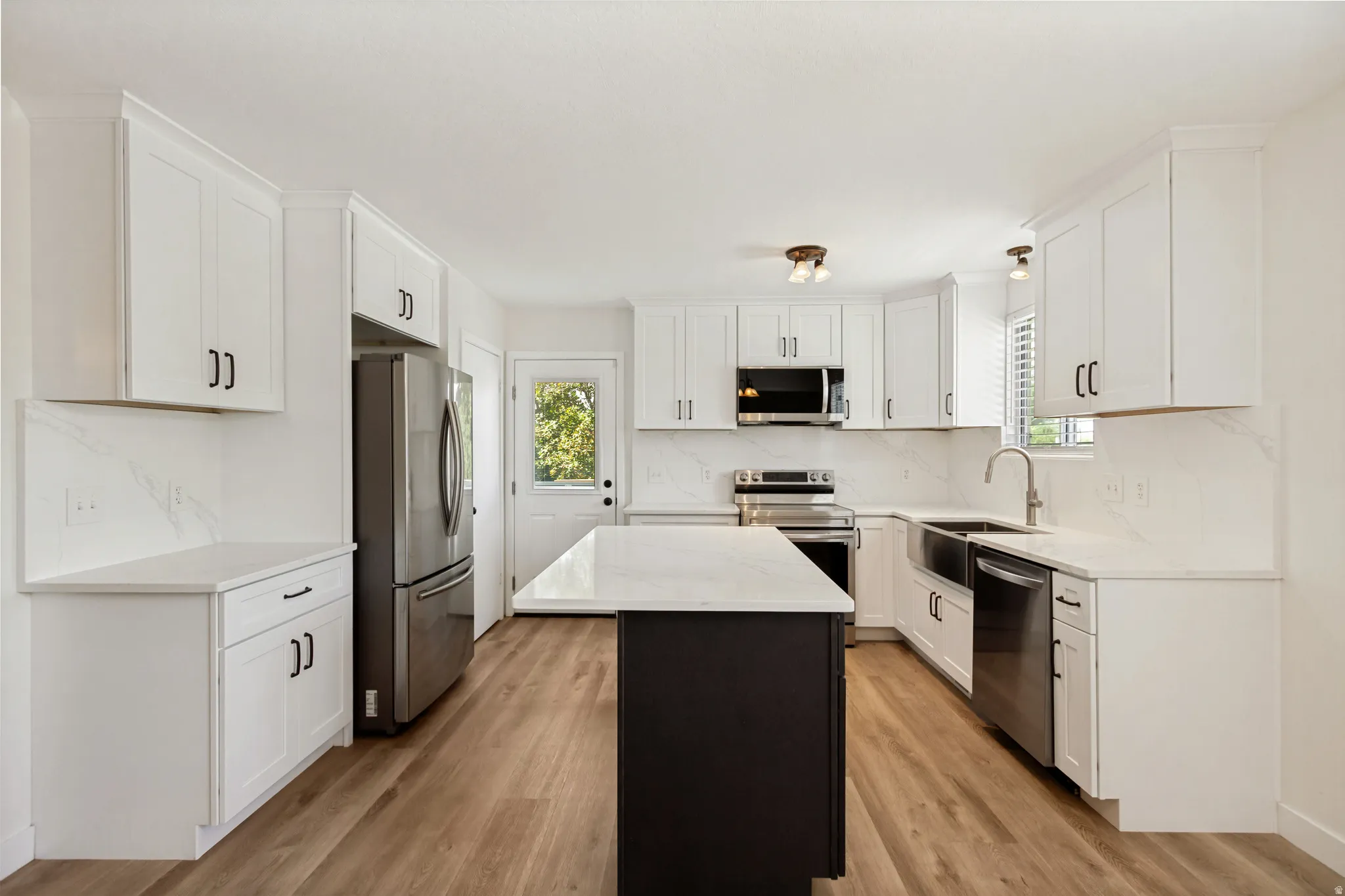 Kitchen featuring white shaker cabinetry, stainless steel appliances, a center island with contrasting base, wood-finish flooring, and white countertops with matching backsplash