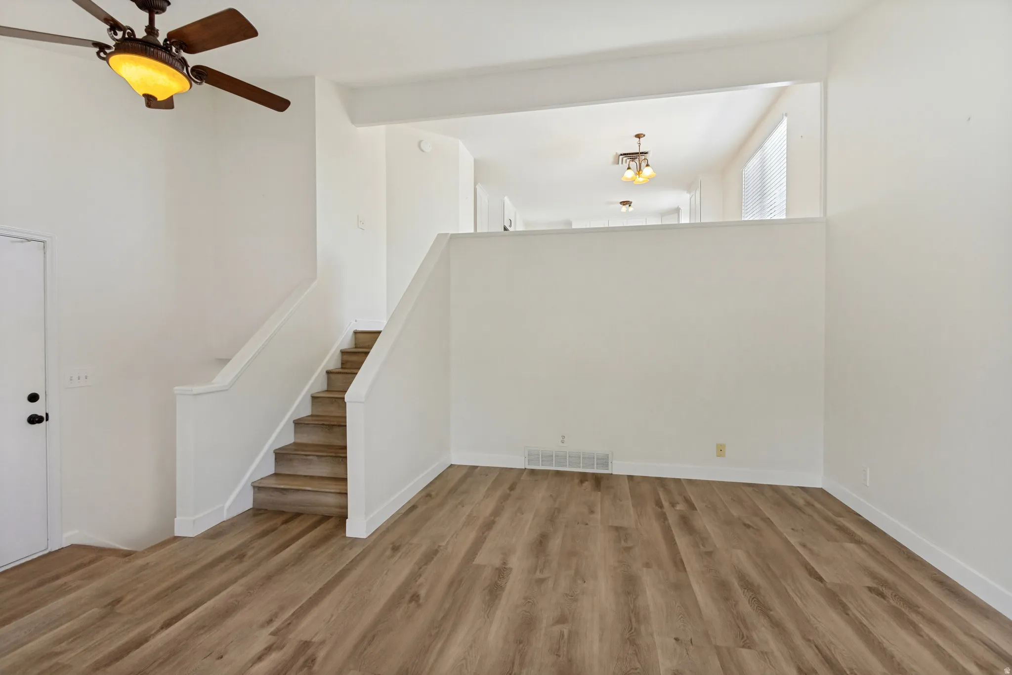 Wood-finish flooring, staircase with white railing, built-in ceiling fan with light fixture, white interior walls, and an open wall cut-out