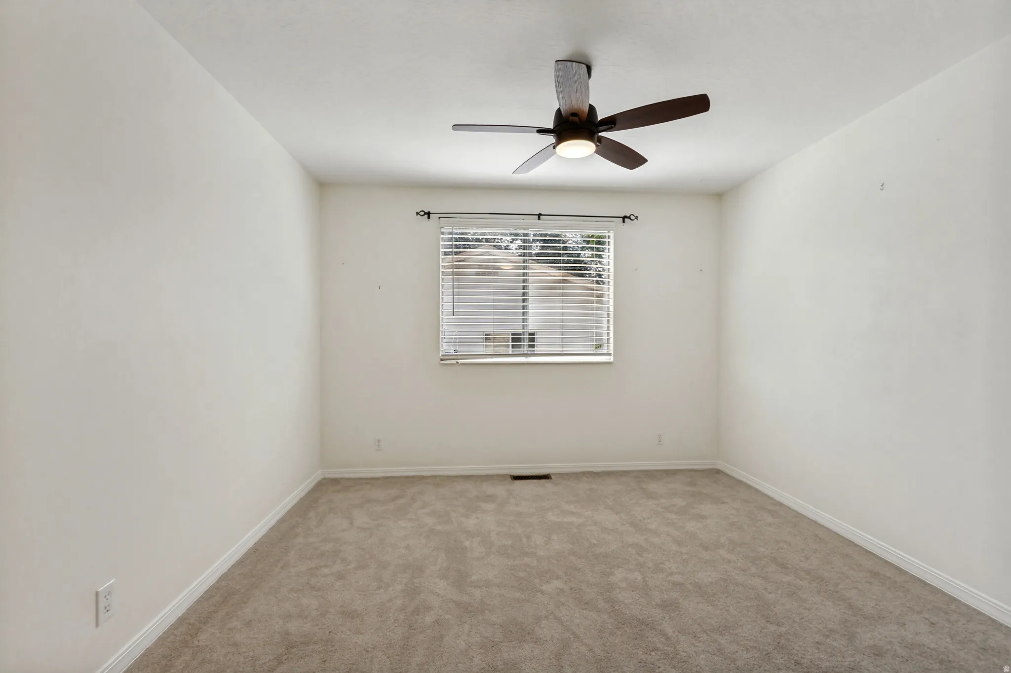 Carpeted room featuring a ceiling fan with integrated lighting and a window with blinds