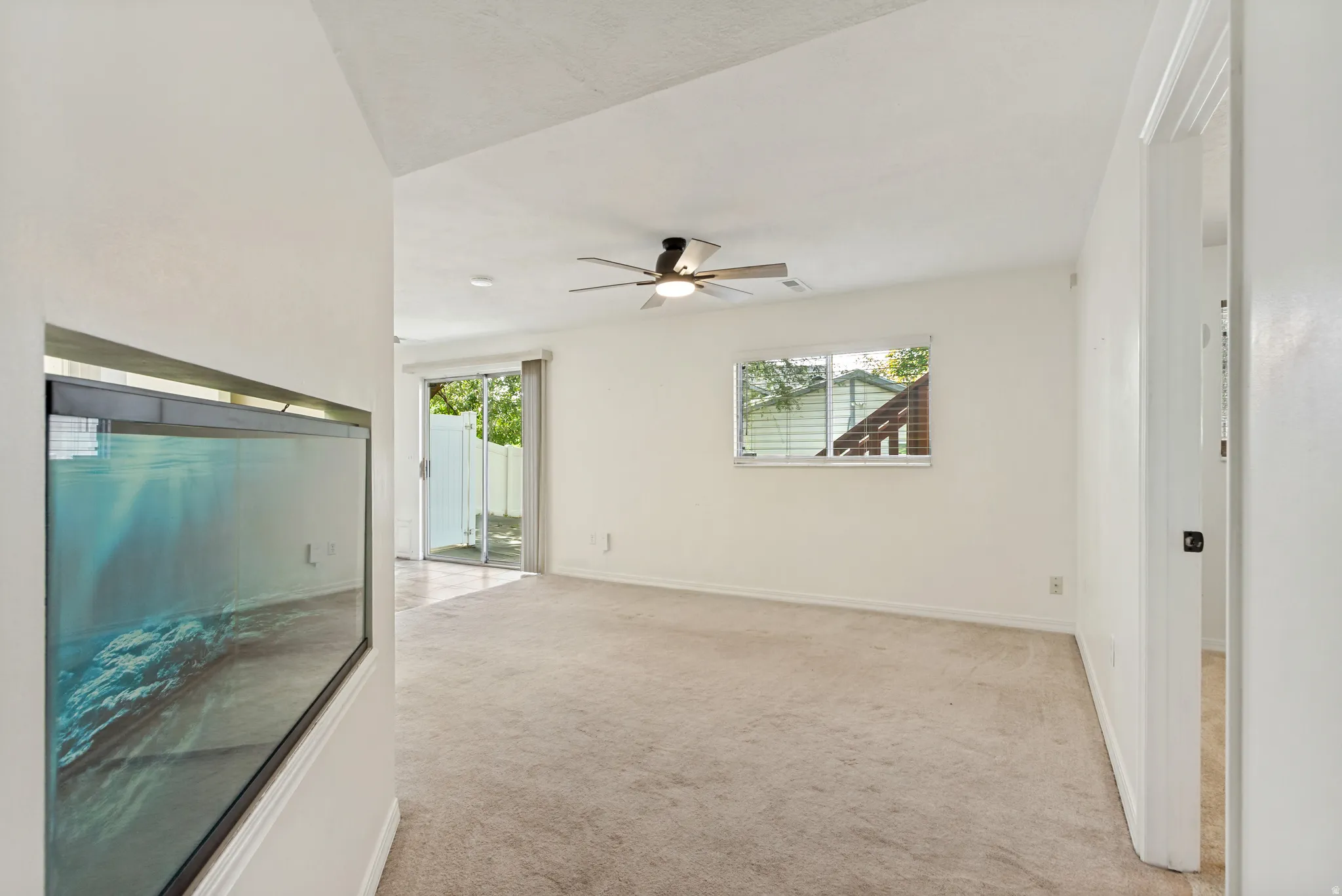 Carpeted flooring, vaulted ceiling, built-in aquarium, ceiling fan, and sliding glass door