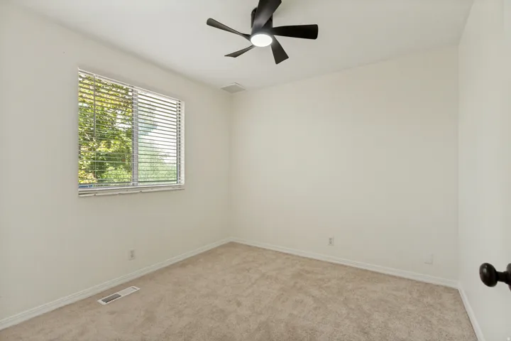 Neutral wall paint, carpeted flooring, window with blinds, and a ceiling fan with integrated lighting