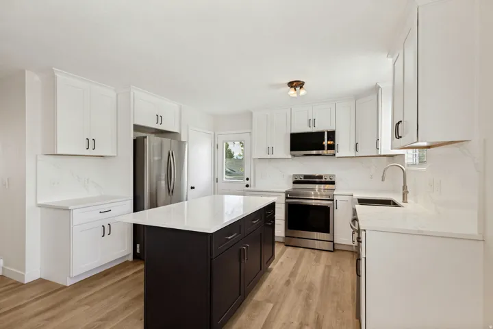 White shaker cabinetry, stainless steel appliances, wood-finish flooring, central island with dark cabinetry, and white countertops