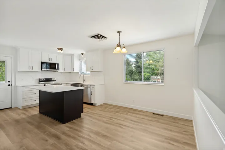 Kitchen featuring an island, stainless steel appliances, wood-finish flooring, white cabinetry, and a window with blinds