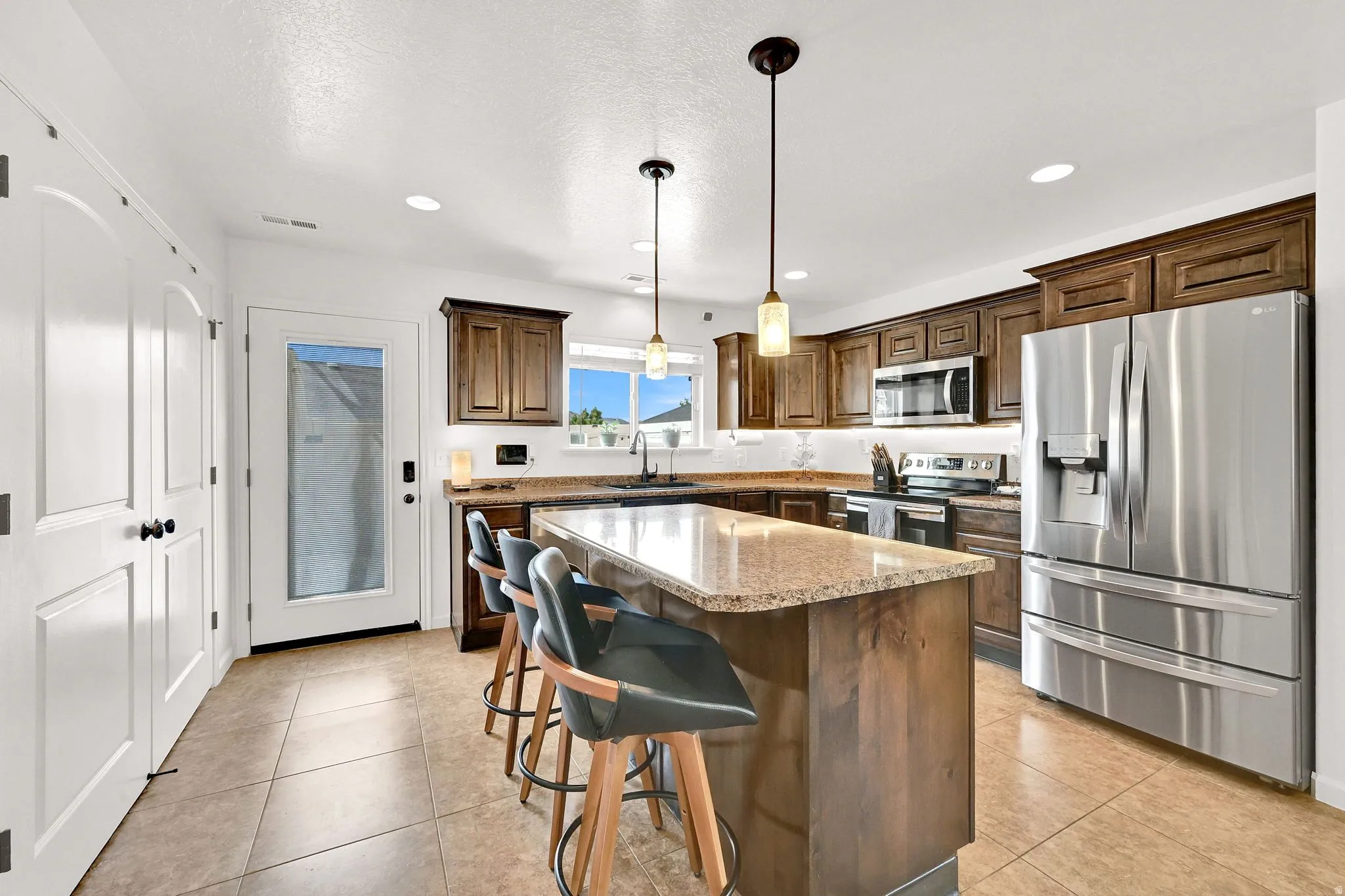Kitchen featuring a large island with stone countertop, stainless steel appliances, dark wood cabinetry, and recessed lighting
