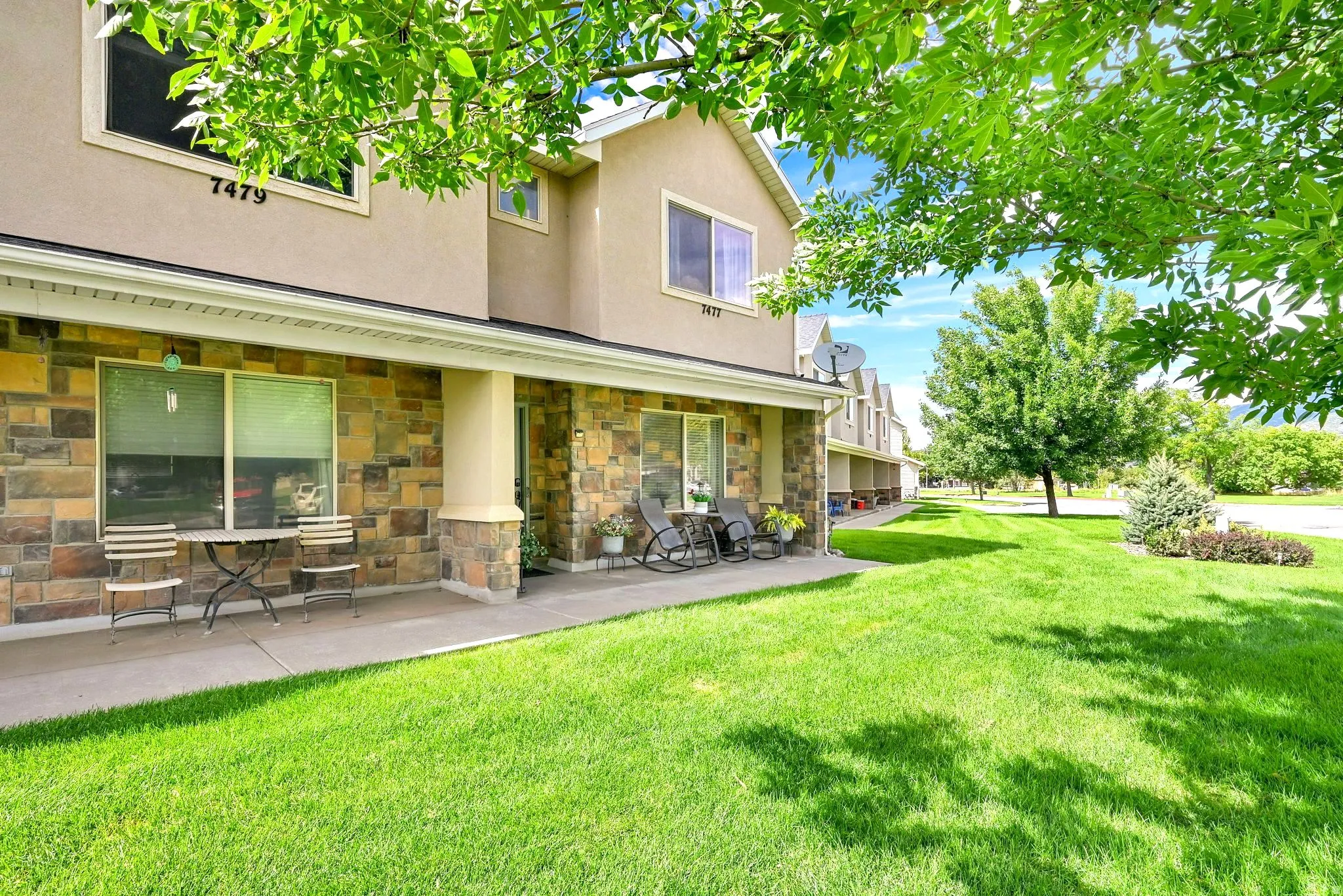 Stucco and stone facade, covered porch, multiple windows, established lawn, and mature trees