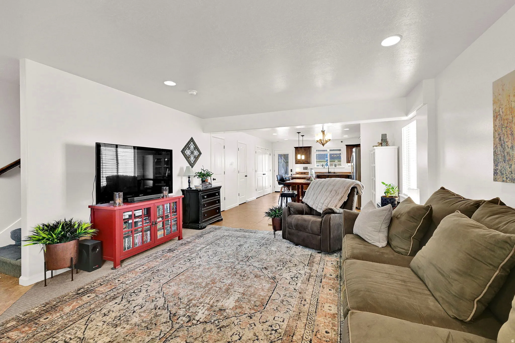 Recessed lighting, wood-finish flooring, white wall finishes, and a visible kitchen beyond
