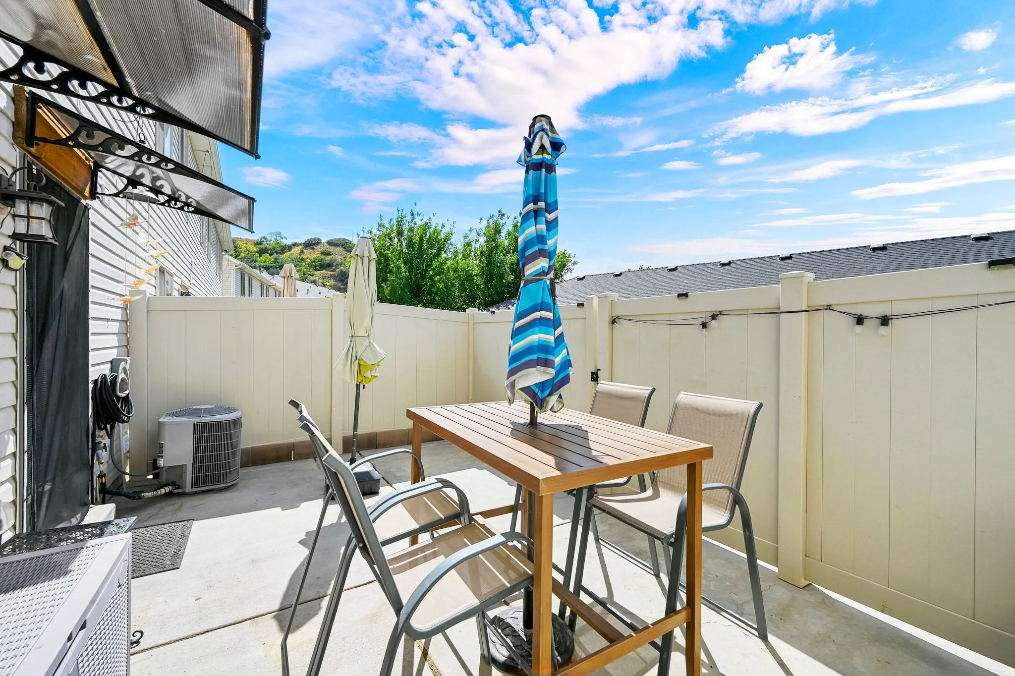 Paved patio featuring a privacy fence, wall-mounted awning, and exterior lighting