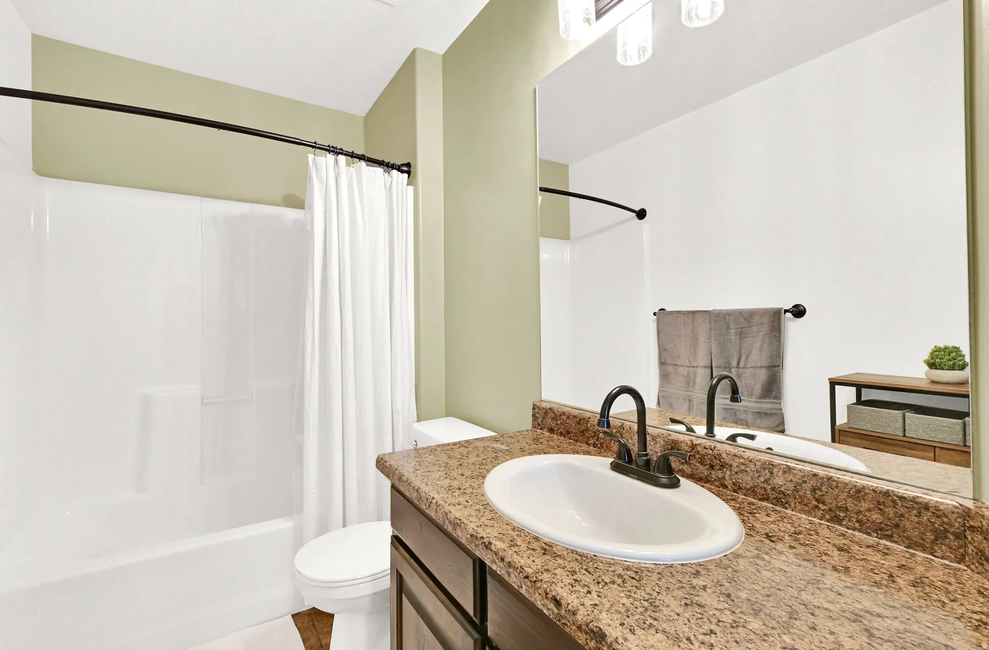 Integrated bathtub and shower combination, vanity with an undermount sink, bronze-finish faucet, and a large wall-mounted mirror