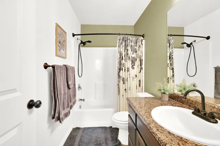 Bathroom featuring a white bathtub with shower, a vanity with a granite-style countertop, a single basin sink, and a framed mirror