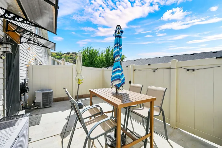 Paved patio featuring a privacy fence, wall-mounted awning, and exterior lighting