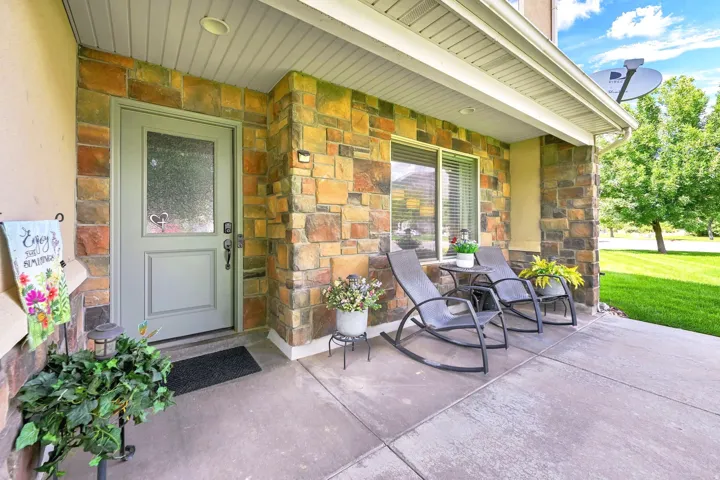 Covered concrete front porch featuring stone veneer accents, a single-light entry door, and a single window with blinds