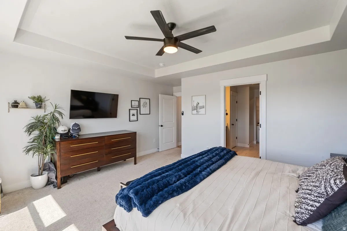 Tray ceiling with a ceiling fan, light gray wall paint, and light-colored carpet flooring