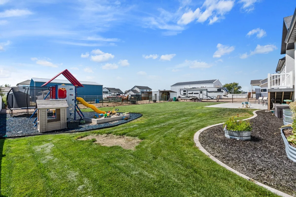 Expansive lawn area, concrete patio, raised garden beds, wood chip landscaping, and a built-in deck with white railings