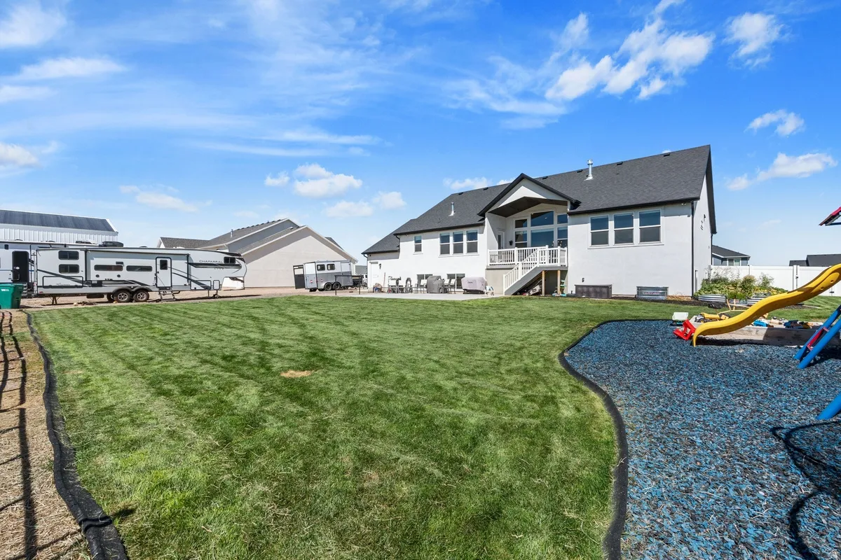 Expansive backyard featuring a lush lawn, white brick exterior, black roof, and a deck with white railings