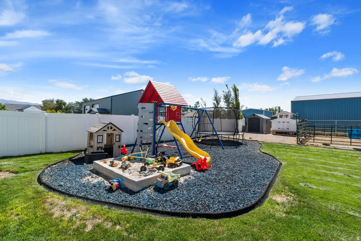 Expansive backyard with a manicured lawn, white privacy fencing, and a dedicated play area featuring a sandbox