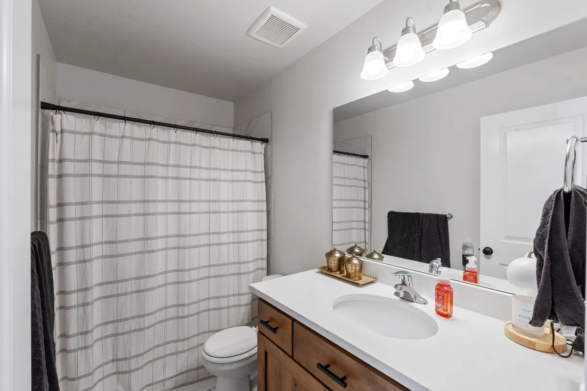 Bathroom featuring a wood-finish vanity with black hardware, a white countertop with an integrated sink, and a wall-mounted mirror with a four-bulb light fixture