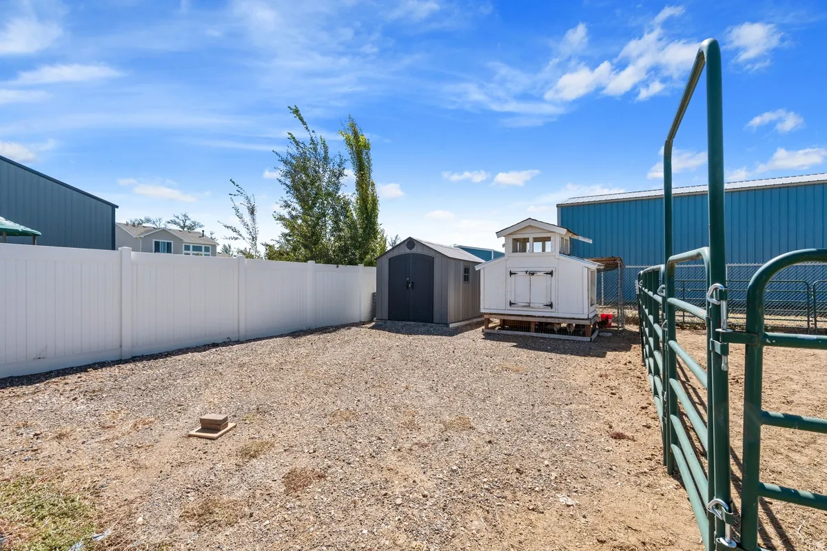 Gravel area featuring a white privacy fence, a storage shed, and a small utility structure