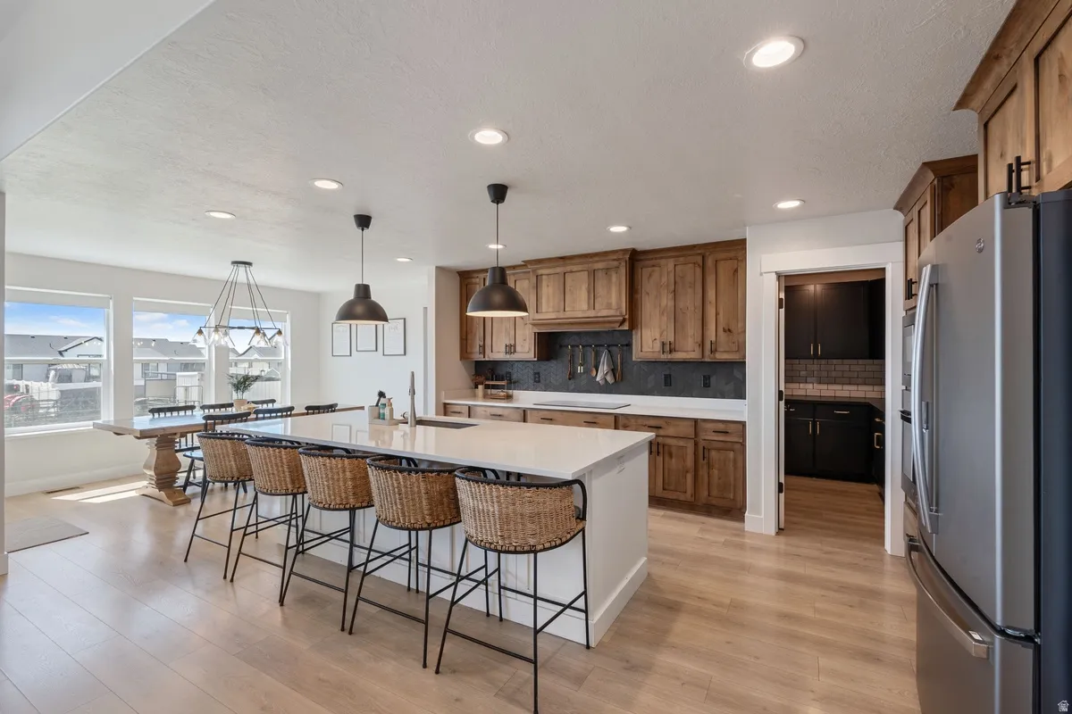 Open-concept kitchen with a large central island, light wood-finish flooring, recessed lighting, and wooden cabinetry
