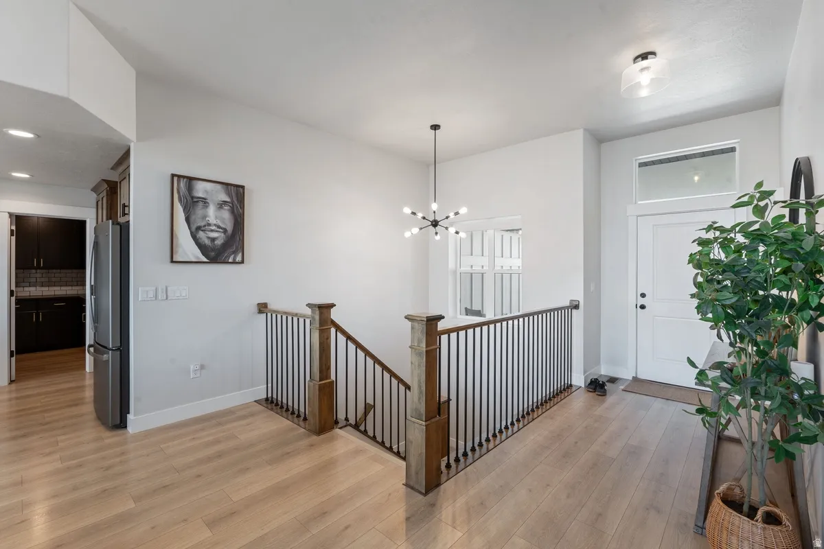 Light wood-finish flooring, white walls, black metal stair railing, white entry door with transom window, and a modern chandelier