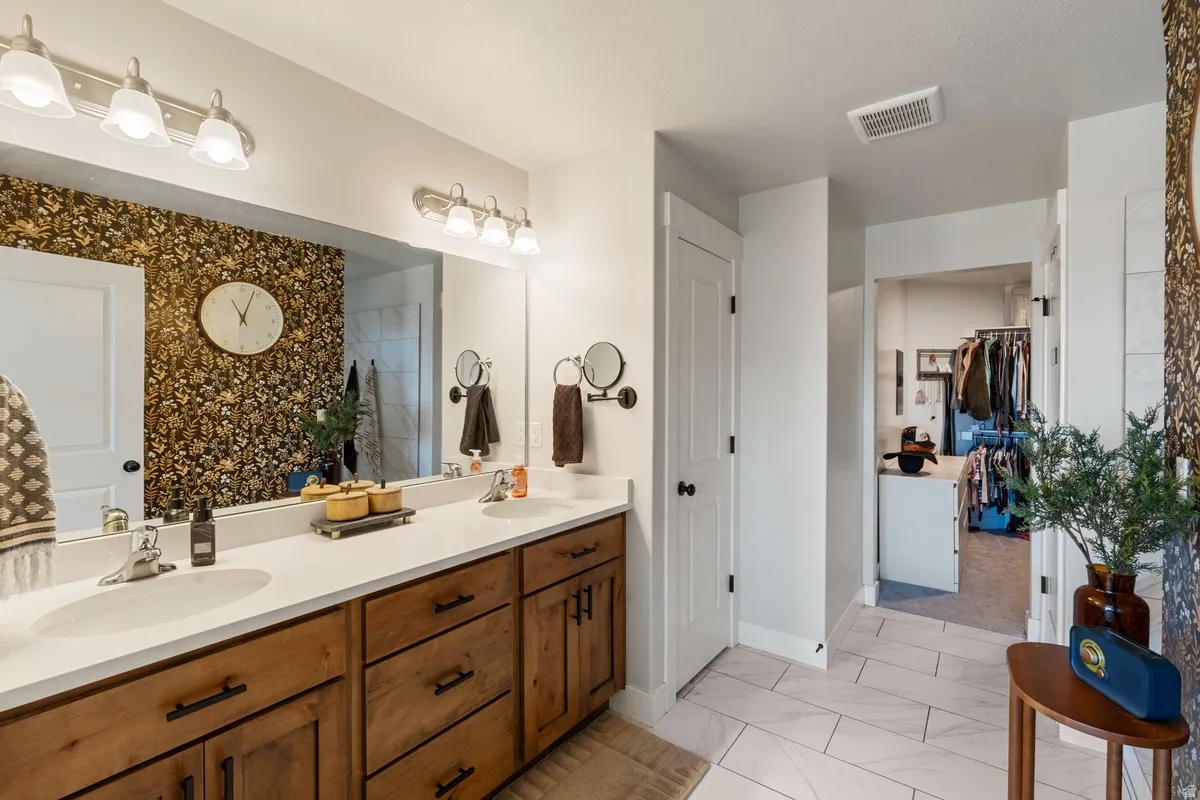 Spacious bathroom featuring a dual vanity with light-colored countertops, wood-finish cabinetry, and a large wall mirror