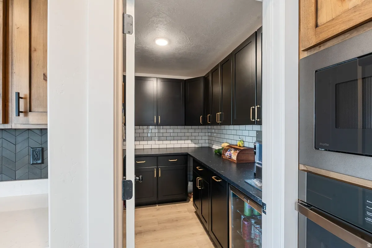 Kitchenette featuring matte black cabinetry, subway tile backsplash, dark countertops, and wood-finish flooring