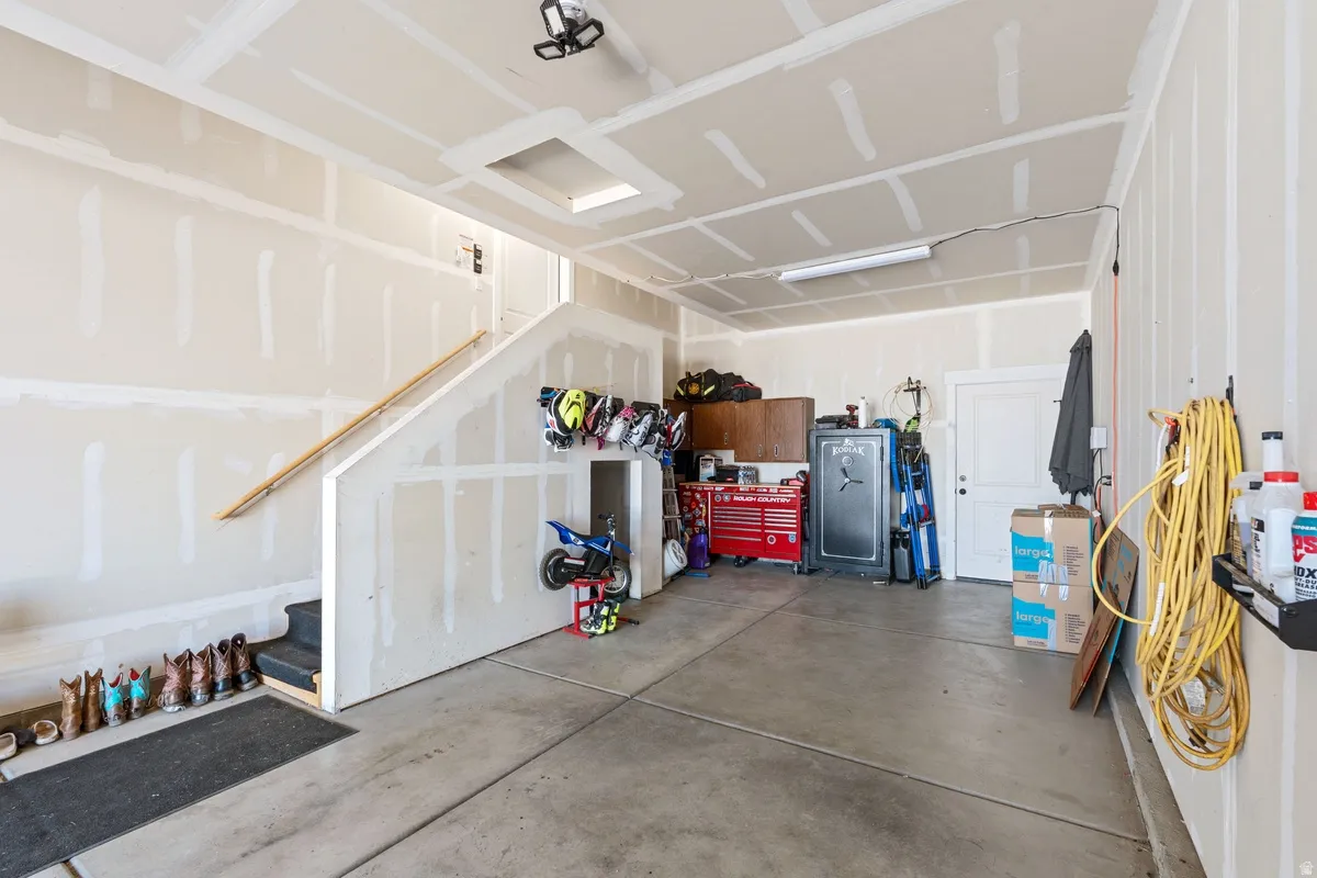 Spacious garage featuring a concrete floor, stairway access, and exposed drywall