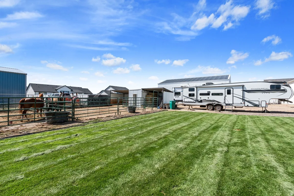 Expansive green lawn, metal fencing, open-air covered structure, additional enclosed structure, and a large metal building