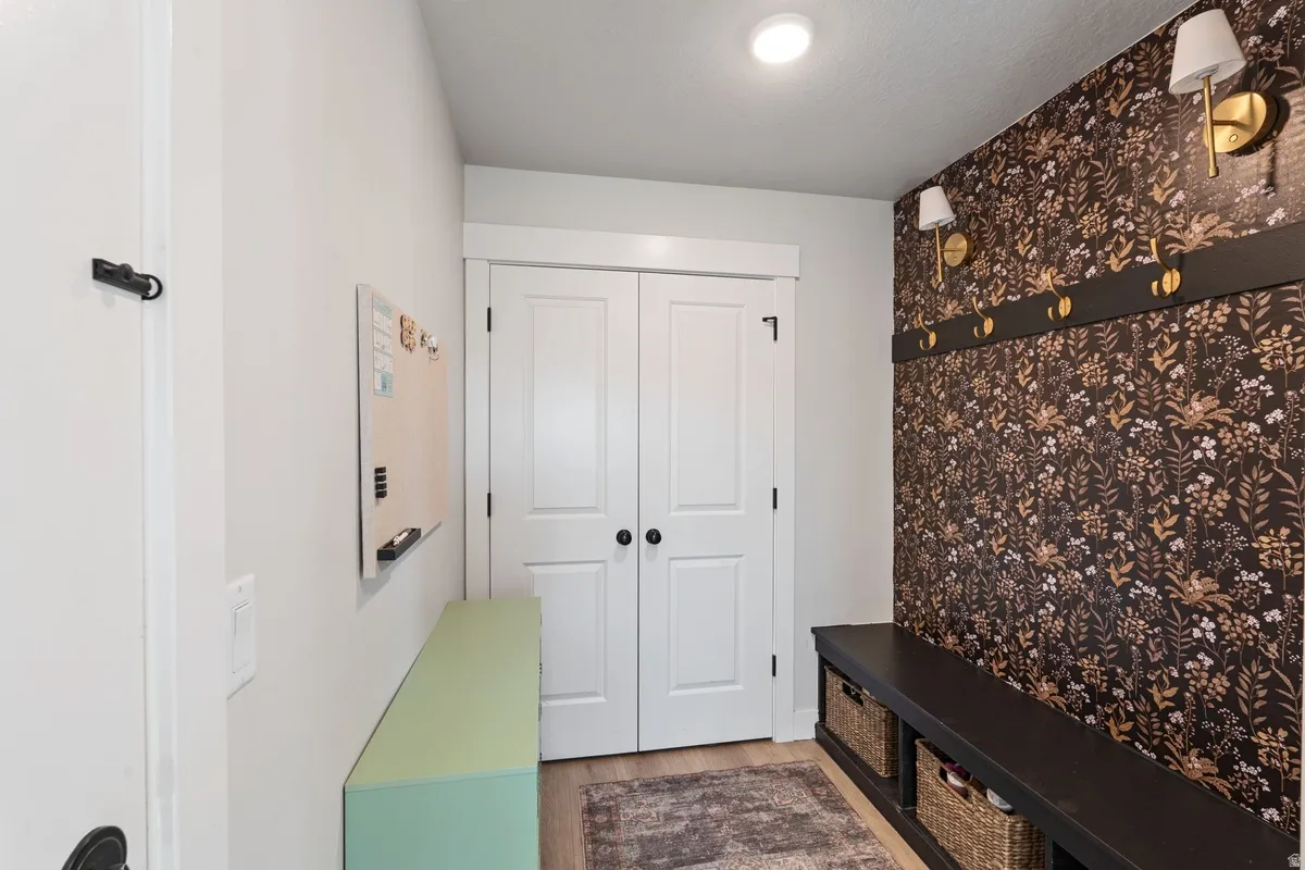 Built-in bench seating with cubbies, accent wall with decorative wallpaper, wall-mounted sconce lighting, and a coat rack with brass hooks