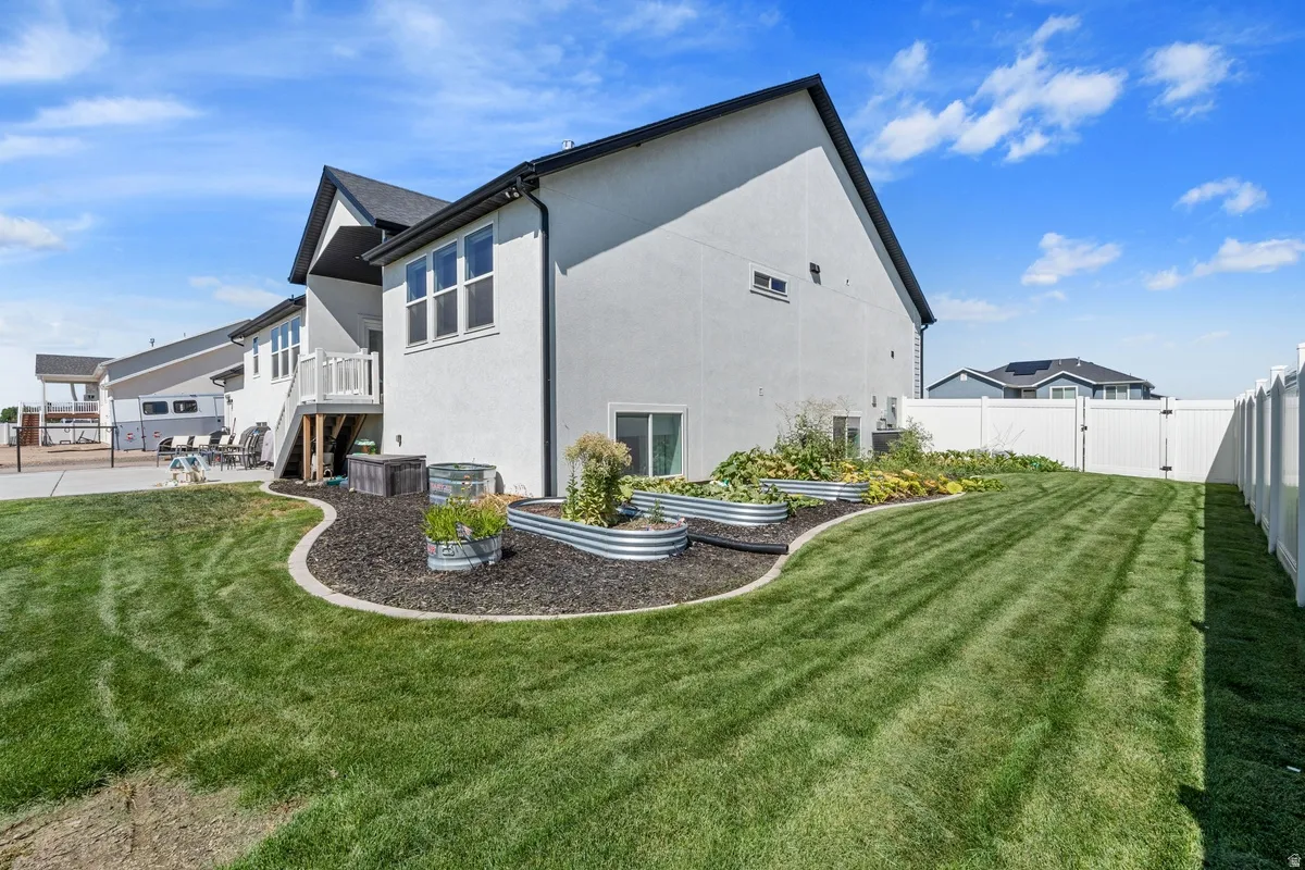 Manicured lawn with a white privacy fence, raised garden beds, and an upper-level deck