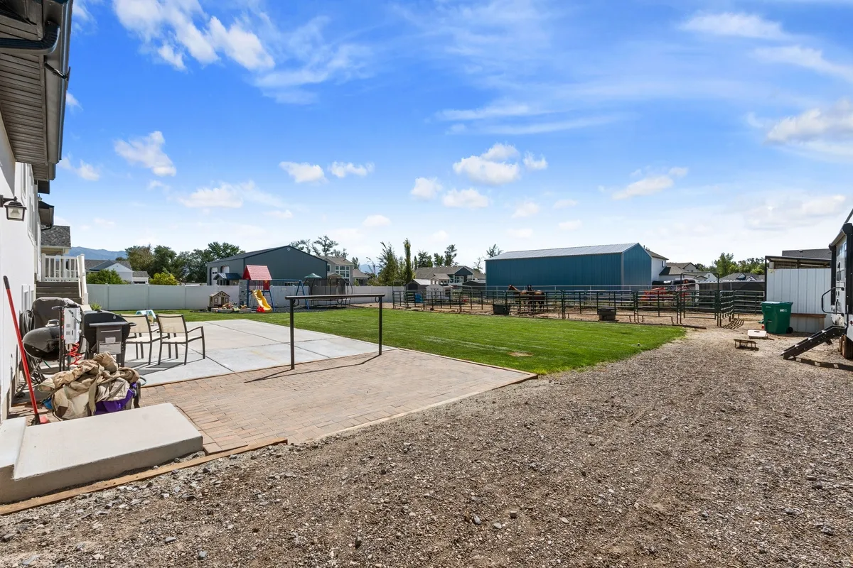 Expansive backyard featuring a large concrete patio, a gravel area, and a green lawn bordered by fencing