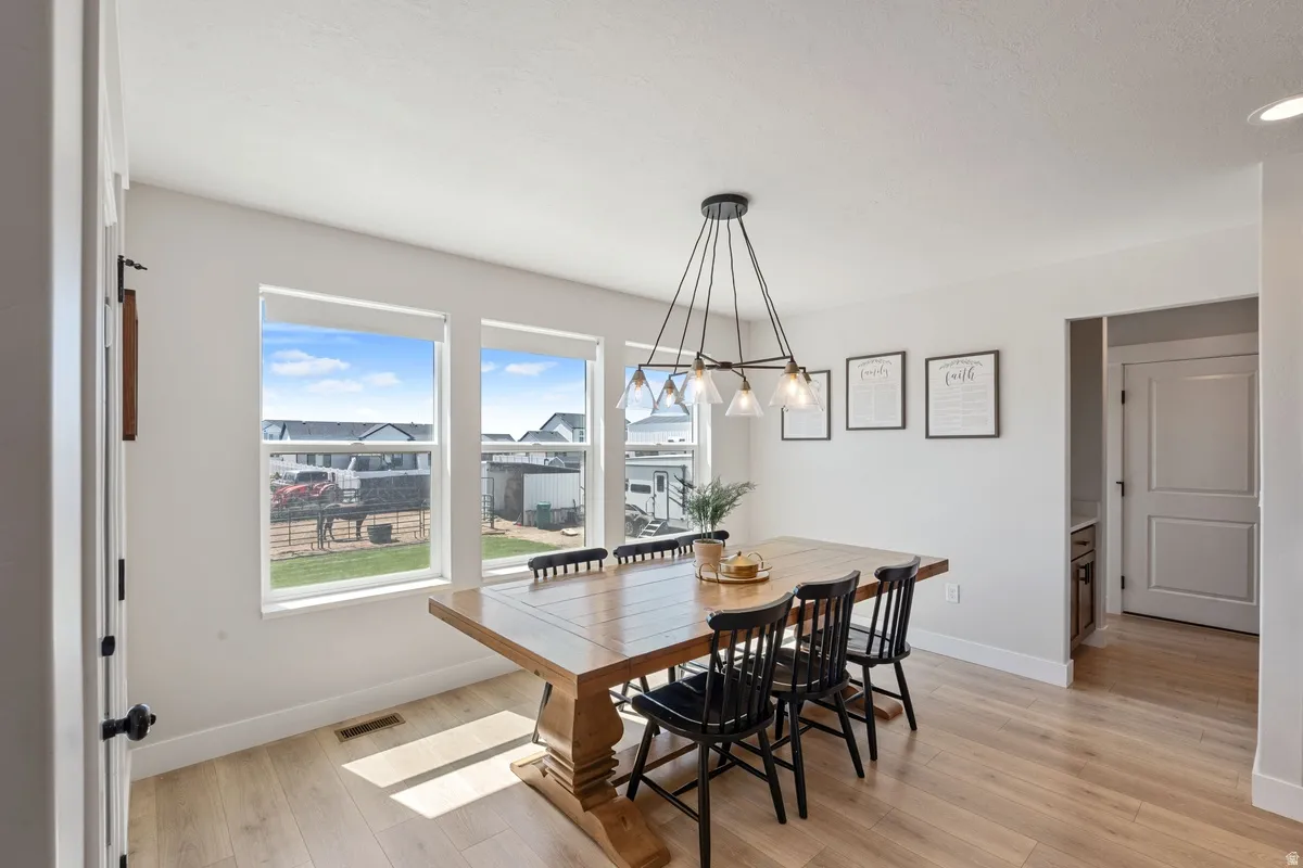 Dining area featuring three large windows, a linear chandelier with glass shades, light wood-finish flooring, and recessed lighting