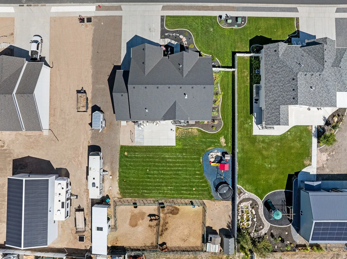 Expansive lot featuring a large main residence with a dark shingle roof, detached auxiliary building, multiple grassy lawn areas, and an animal enclosure