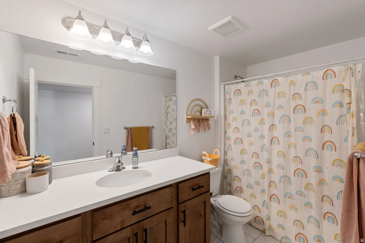 Bathroom featuring a wood-finish vanity with a white countertop, an integrated sink, a rectangular mirror, and a shower with a white tile surround