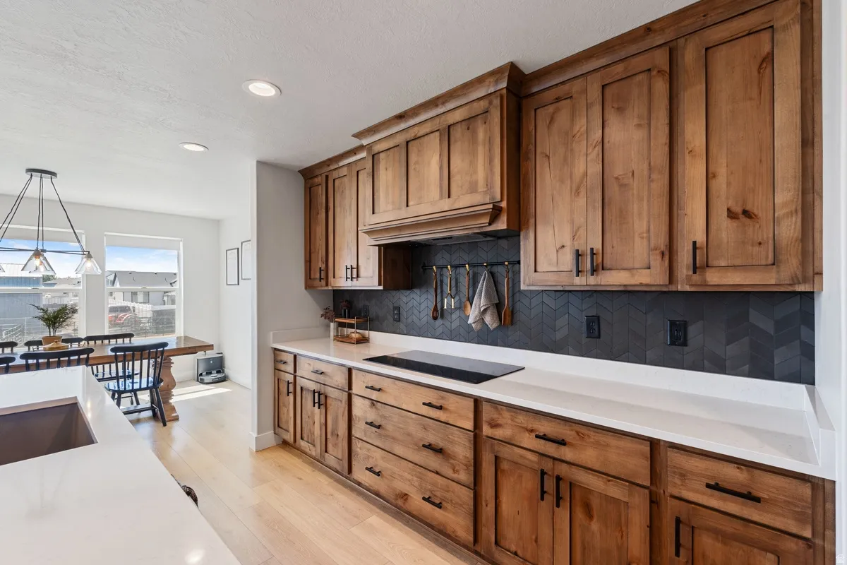 Wood cabinetry with dark hardware, white countertops, and a dark chevron-patterned backsplash