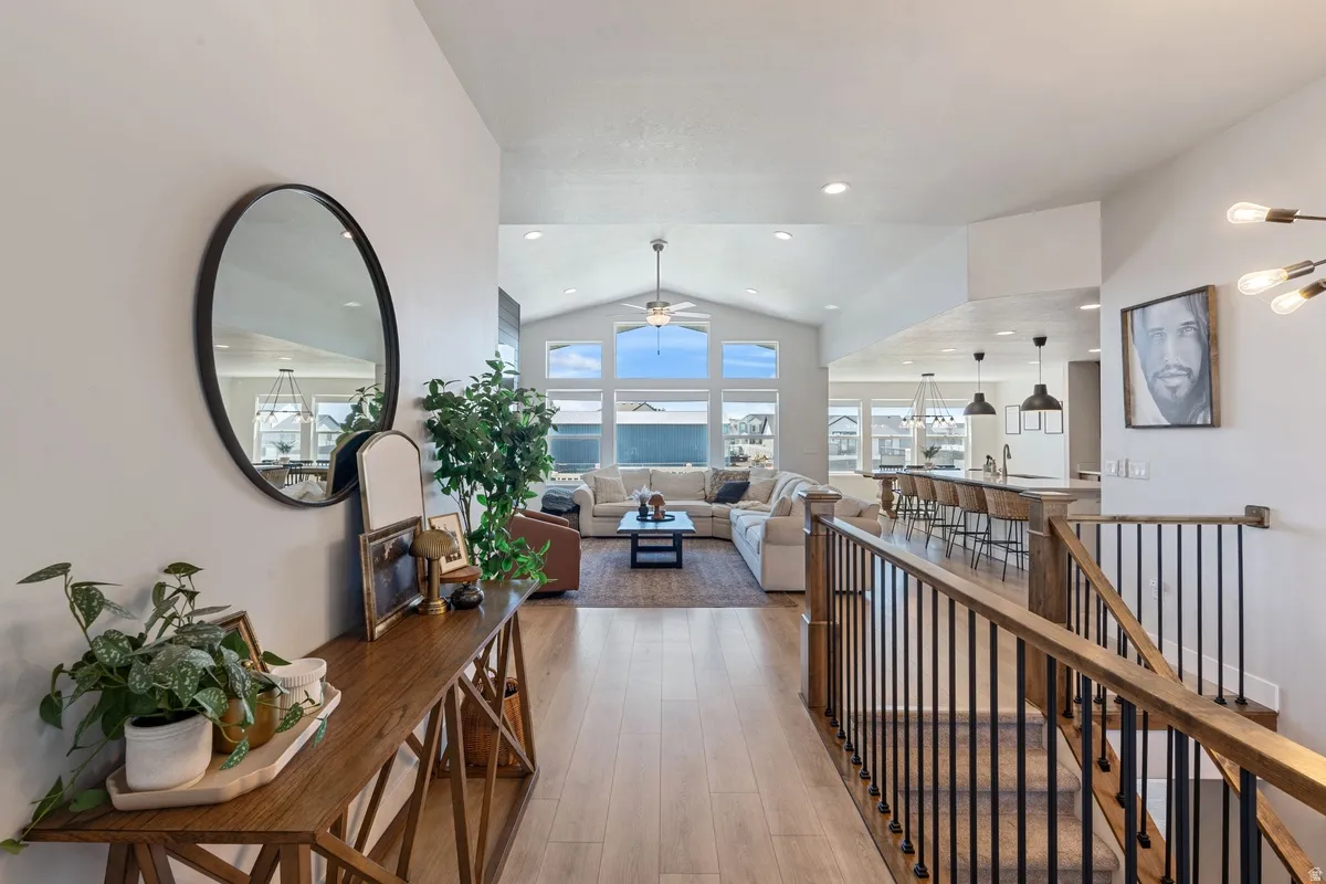 Vaulted ceiling with transom windows, wood-finish flooring, staircase with metal balusters, kitchen island with pendant lighting, and recessed ceiling lights