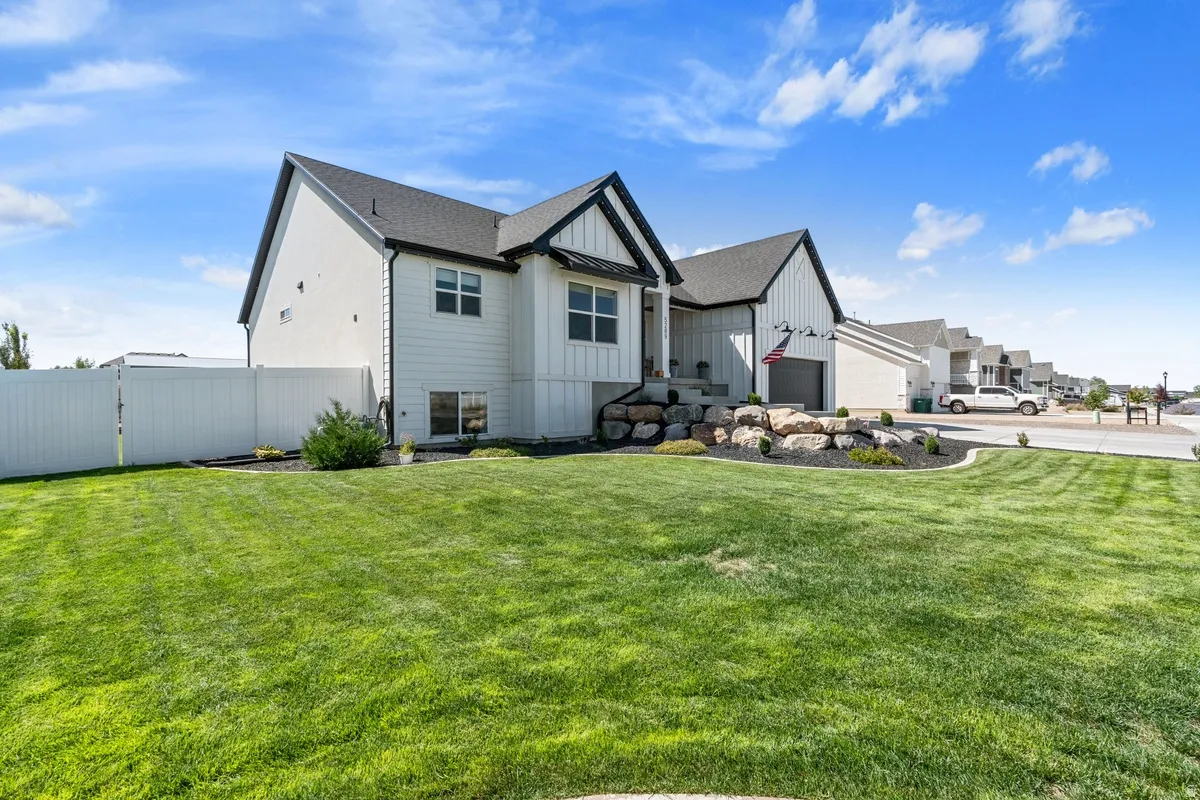White board and batten siding, black trim accents, attached garage, rock landscaping, and a manicured lawn