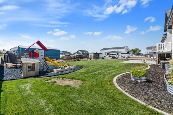 Expansive lawn area, concrete patio, raised garden beds, wood chip landscaping, and a built-in deck with white railings