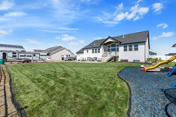 Expansive backyard featuring a lush lawn, white brick exterior, black roof, and a deck with white railings