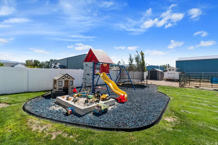 Expansive backyard with a manicured lawn, white privacy fencing, and a dedicated play area featuring a sandbox