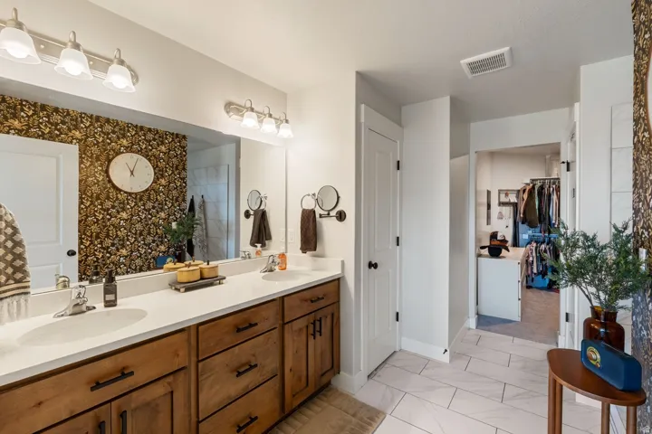 Spacious bathroom featuring a dual vanity with light-colored countertops, wood-finish cabinetry, and a large wall mirror