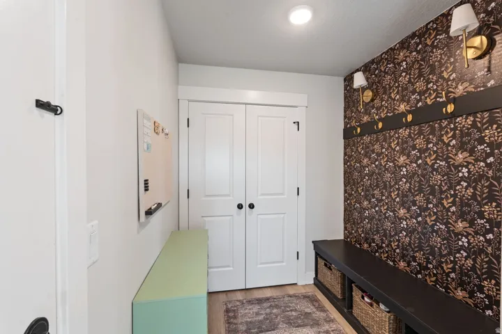 Built-in bench seating with cubbies, accent wall with decorative wallpaper, wall-mounted sconce lighting, and a coat rack with brass hooks