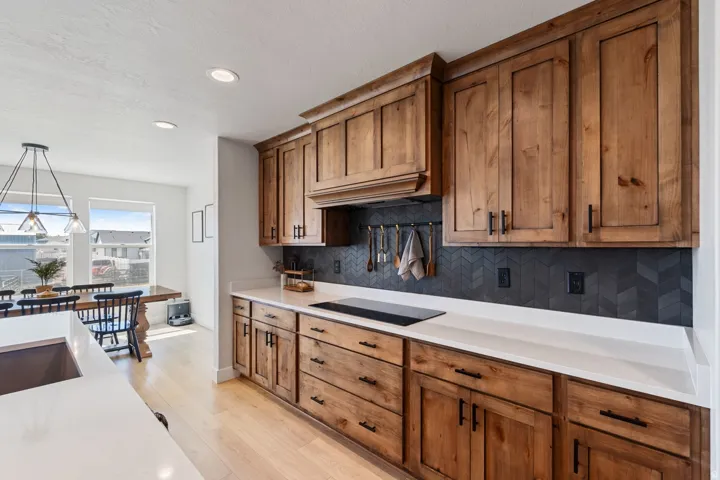 Wood cabinetry with dark hardware, white countertops, and a dark chevron-patterned backsplash